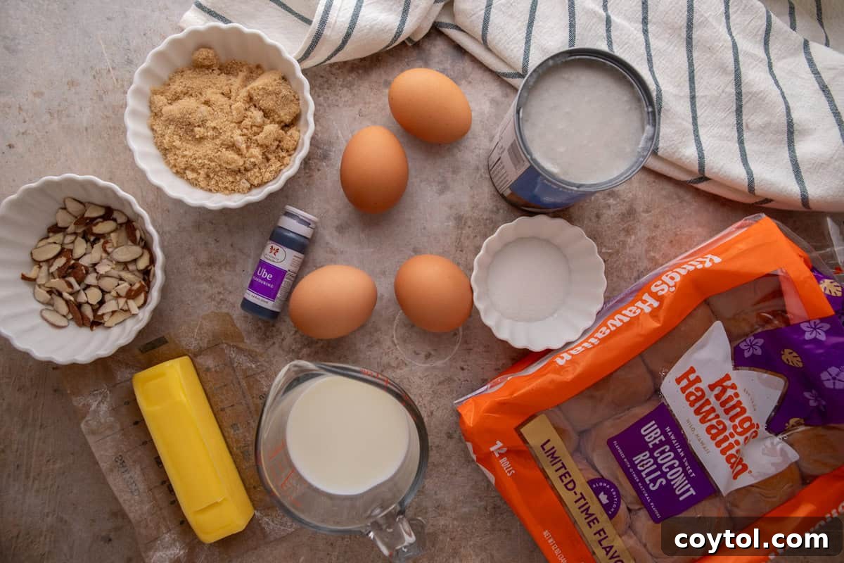 Ingredients for ube French toast bake arranged on a surface: King's Hawaiian Ube Coconut rolls, eggs, a can of coconut milk, brown sugar, butter, a bottle of ube extract, and sliced almonds.