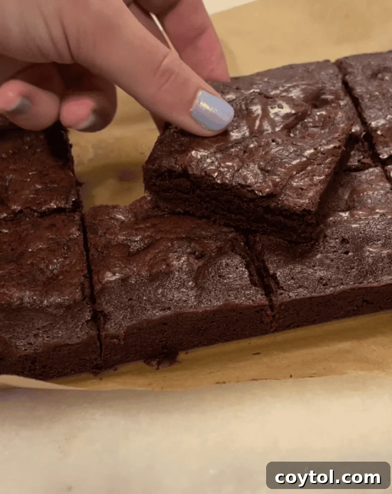 Hand reaching for a fudgy chocolate brownie square cut on parchment paper for Loaf BakeClub