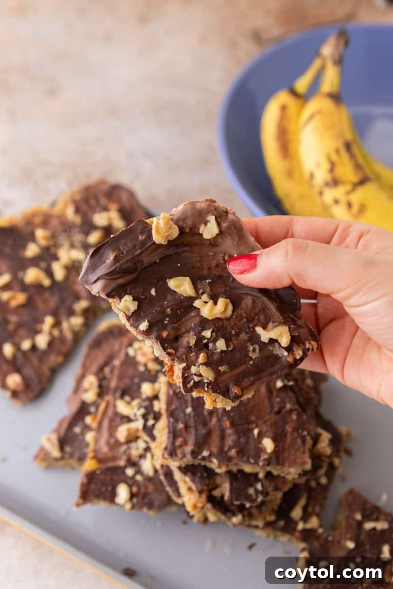 Holding a piece of banana bread Christmas crack topped with chocolate, walnuts, and flaky sea salt.
