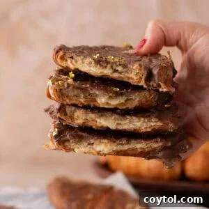 Hand holding a tall stack of croissant Christmas crack pieces with visible flaky layers and gold leaf