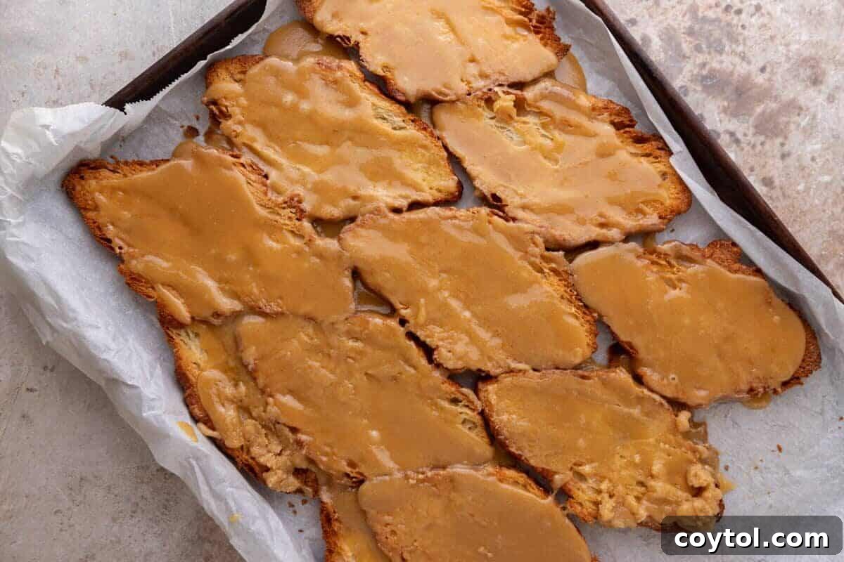 Brown sugar toffee spread over toasted pressed croissants on a parchment-lined sheet pan
