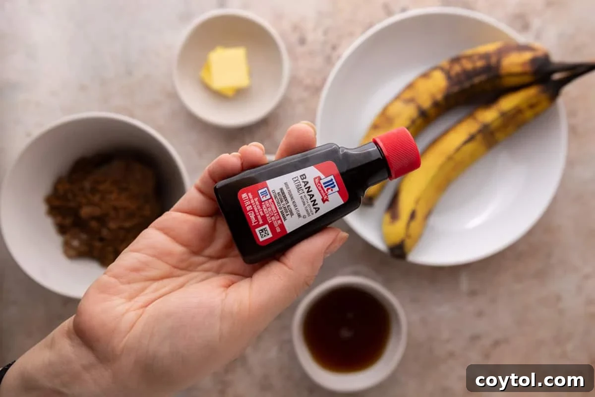 Hand holding a bottle of McCormick banana extract over the banana bread syrup ingredients