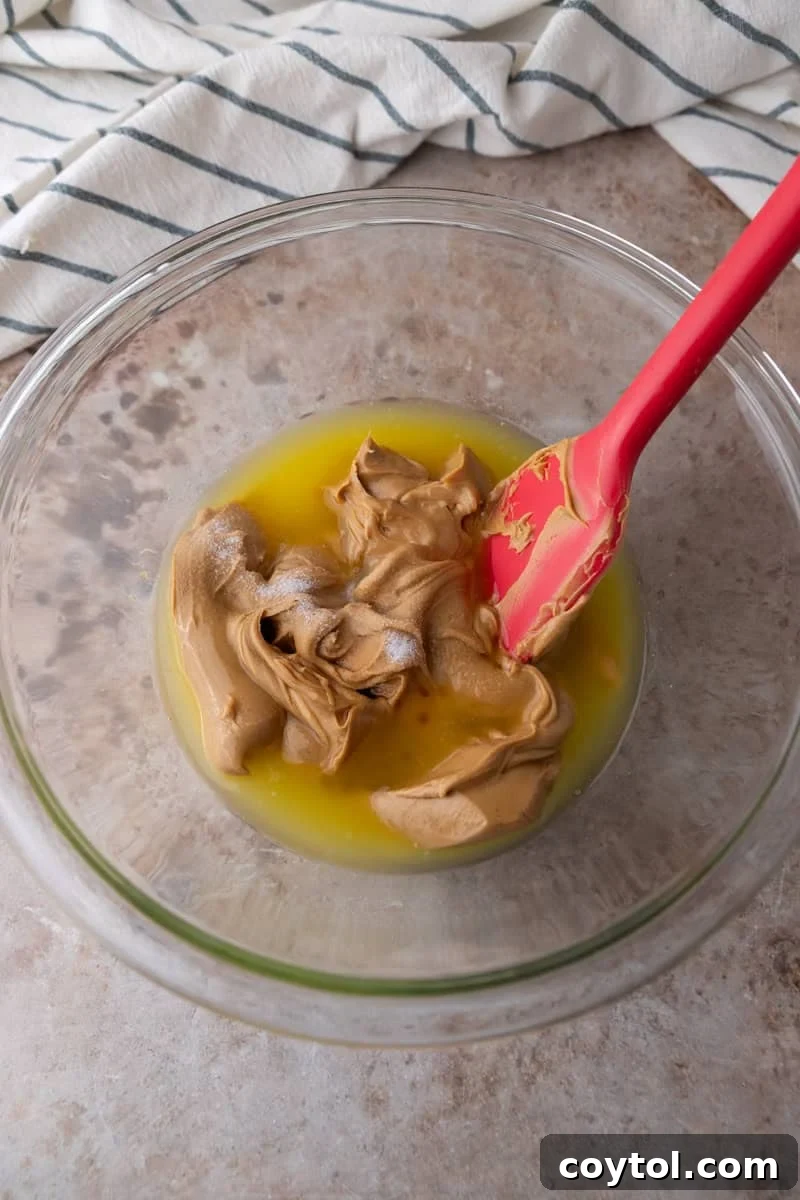 Melted butter and creamy peanut butter in a glass bowl with a red spatula