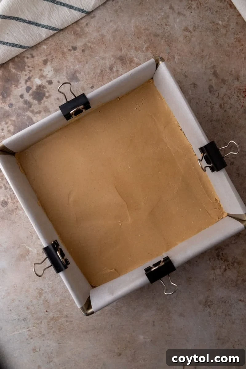 Peanut butter buckeye fudge layer pressed into a parchment lined square pan