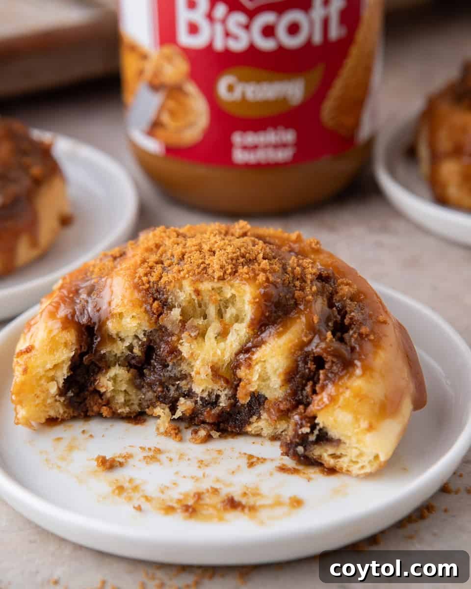 Cookie butter cinnamon roll on a white plate with a bite taken, showing the gooey Biscoff swirl inside