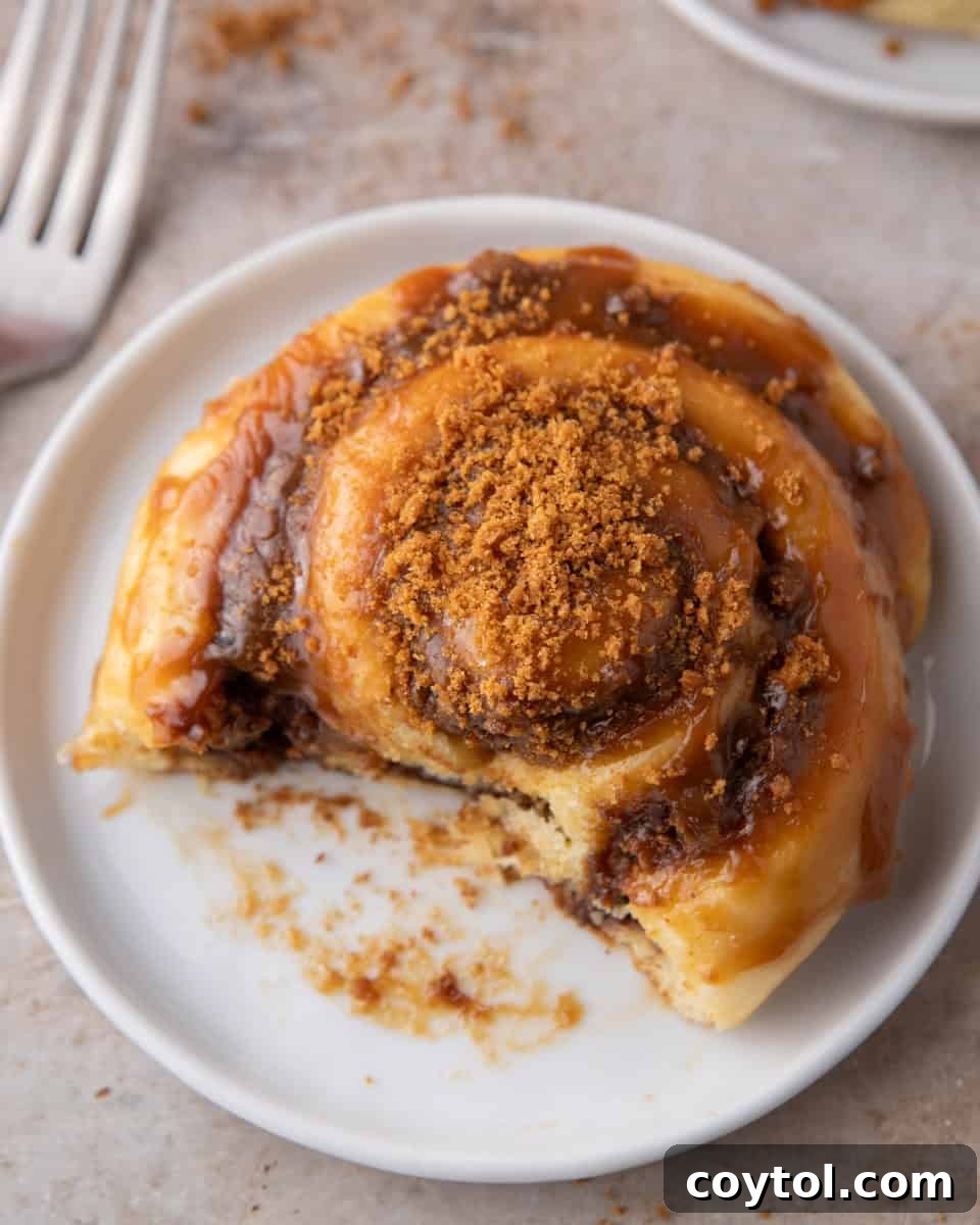 Glazed Biscoff cinnamon roll on a white plate with a bite taken and crushed cookies on top