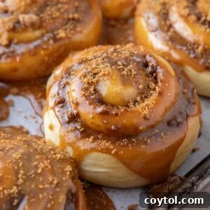 Cookie butter cinnamon roll topped with molten Biscoff glaze dripping down the sides on a sheet pan