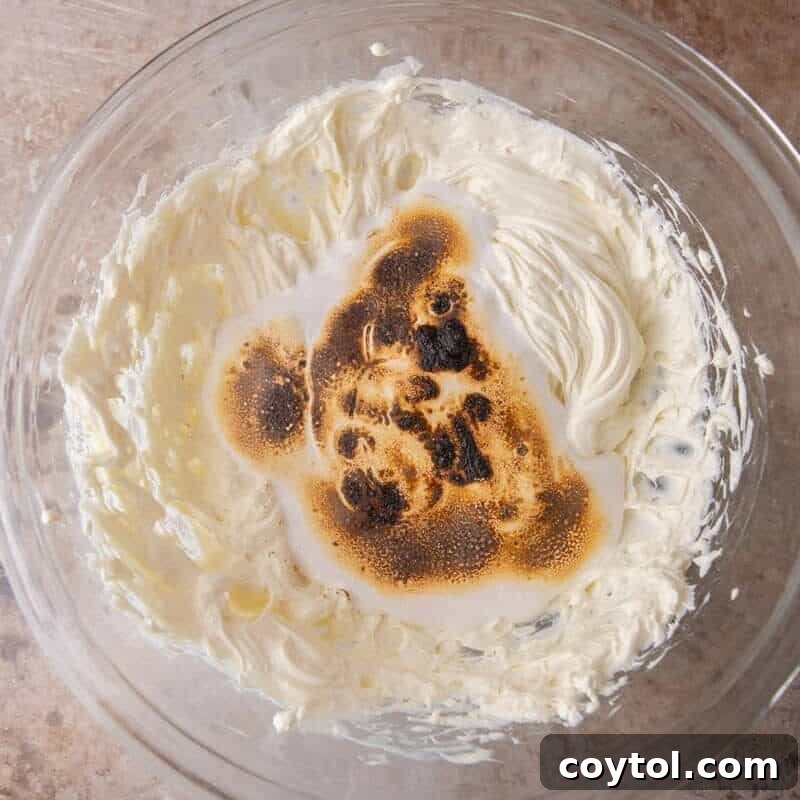 Toasted marshmallow being whipped into beaten cream cheese for the s'mores cheesecake bar filling