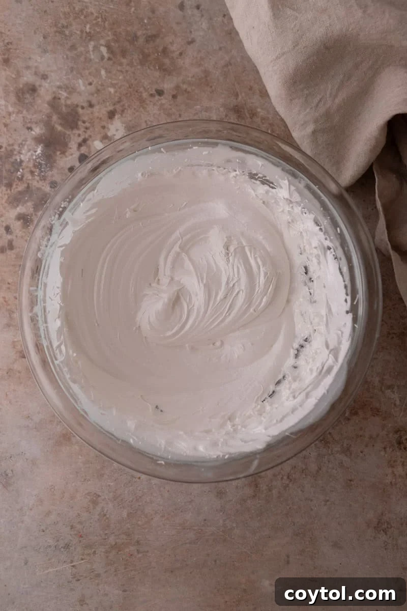 Whipped Swiss meringue with glossy stiff peaks in a glass bowl