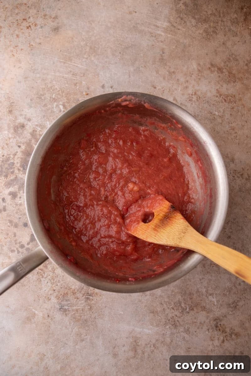 Thick jammy rhubarb filling cooked down in a saucepan with a wooden spoon, deep pink and glossy
