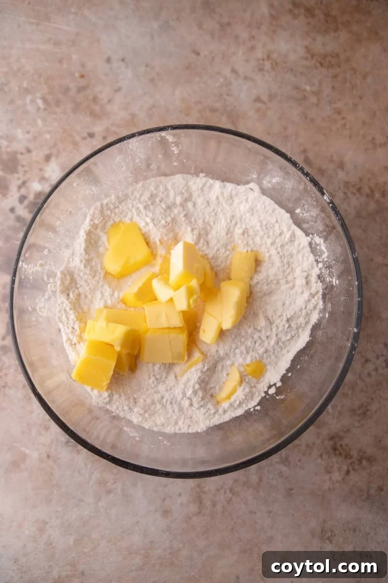 Cold cubed butter added to flour and sugar mixture in a large glass bowl to make shortbread dough