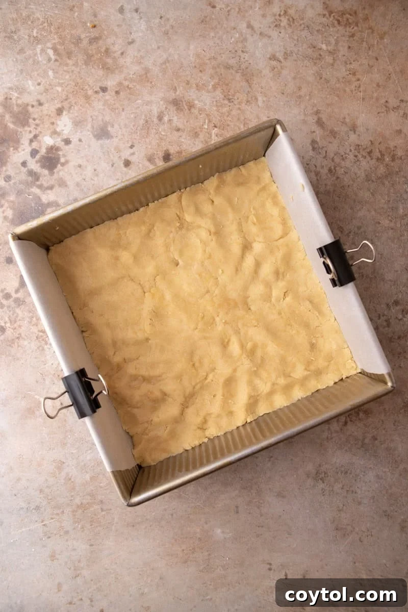 Shortbread dough pressed evenly into the bottom of a parchment-lined 8x8 gold baking pan before par-baking