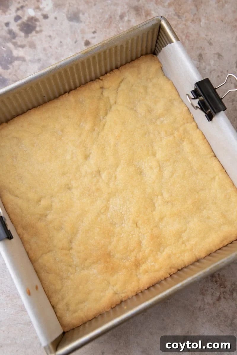 Par-baked shortbread crust in an 8x8 gold baking pan, golden and set, fresh out of the oven