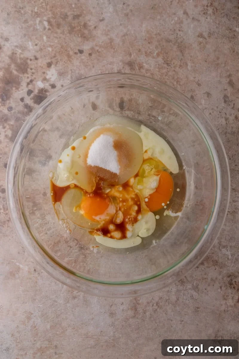 Eggs, sugar, vegetable oil, buttermilk, and vanilla extract combined in a glass mixing bowl before whisking