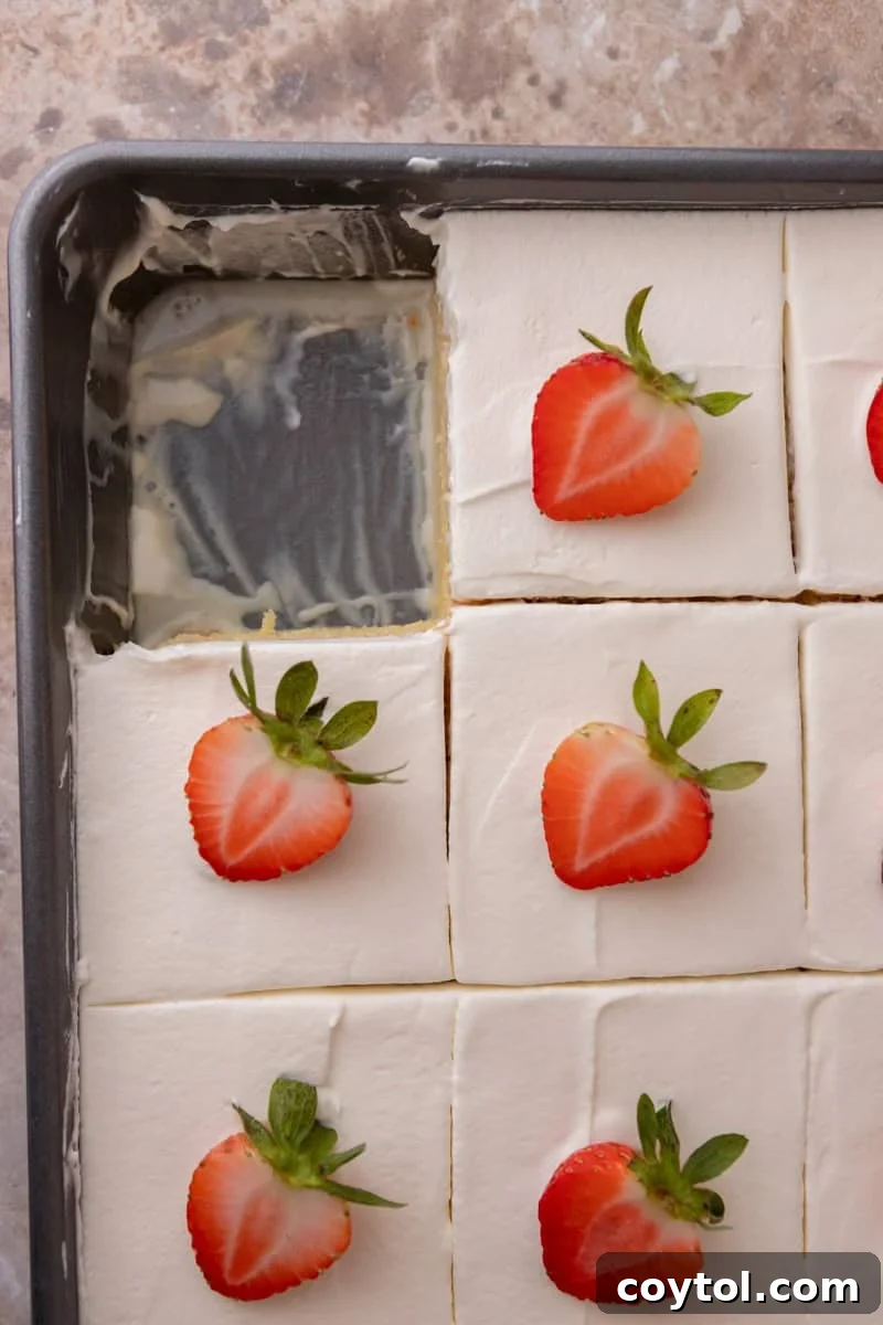Tres leches cake cut into squares and topped with strawberries in the pan