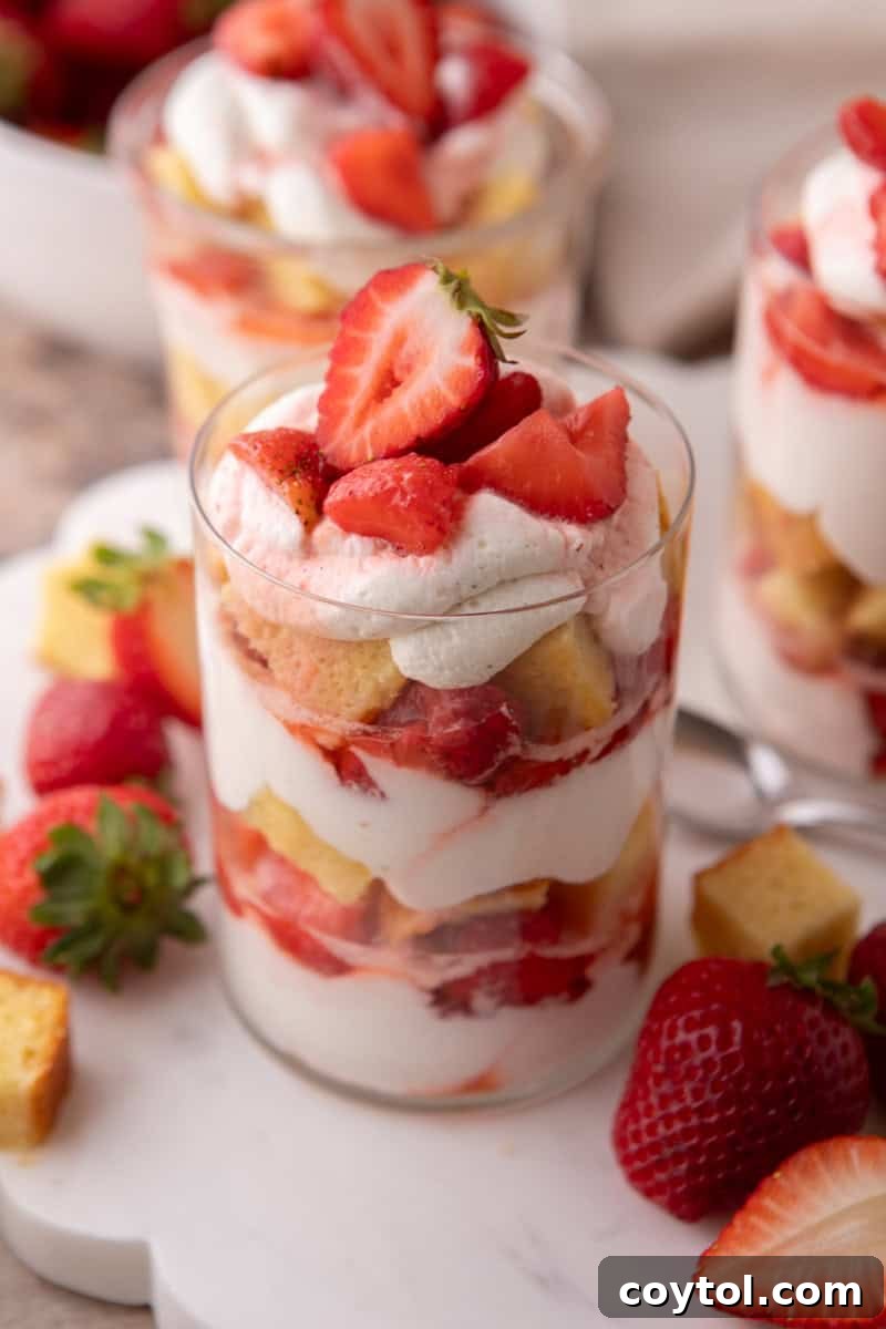 Strawberry shortcake trifle cups in clear glasses topped with whipped cream and a halved strawberry.