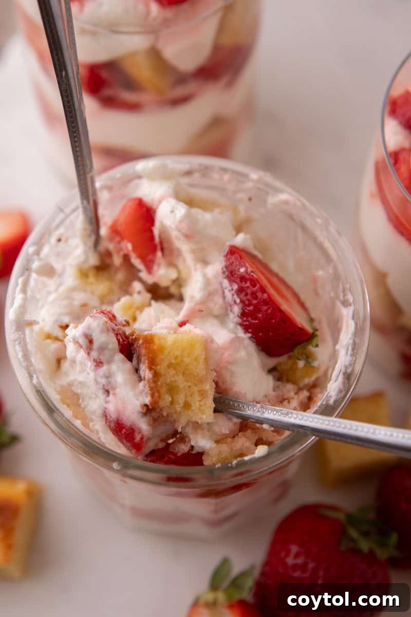 Overhead view of a spoon digging into a strawberry shortcake trifle cup with visible cake cubes and berries