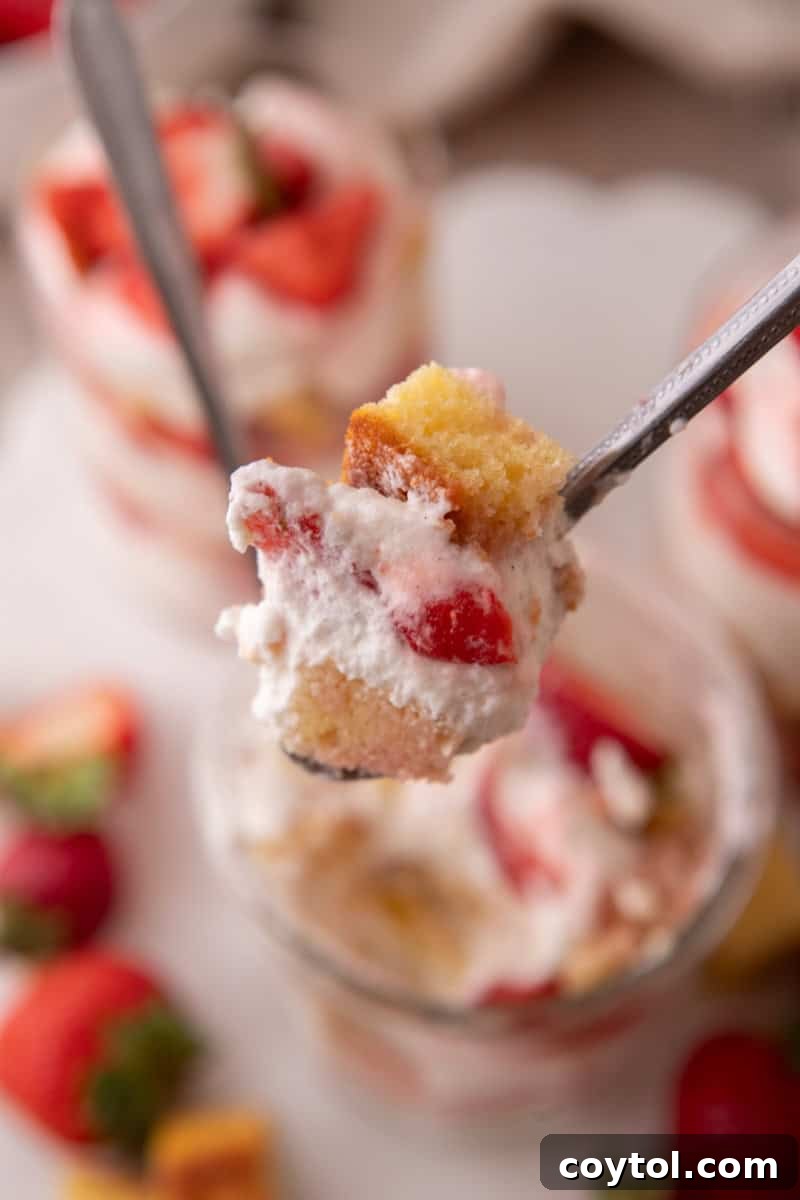 A spoonful of strawberry shortcake trifle with vanilla cake, whipped cream, and juicy strawberries lifted from the glass