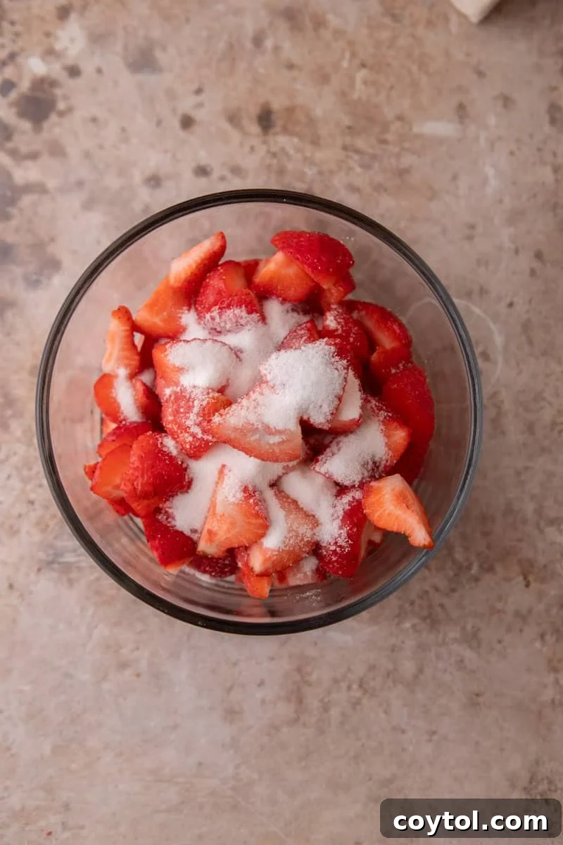 Diced fresh strawberries tossed with granulated sugar in a glass bowl.