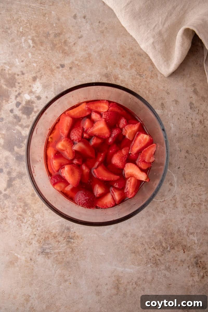 Macerated strawberries sitting in their own ruby red syrup in a glass bowl.