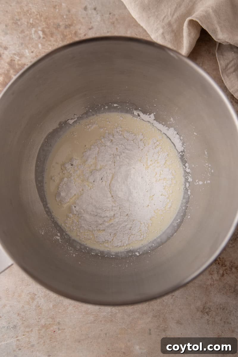 Cold heavy cream and powdered sugar in a stainless steel mixing bowl before whipping.