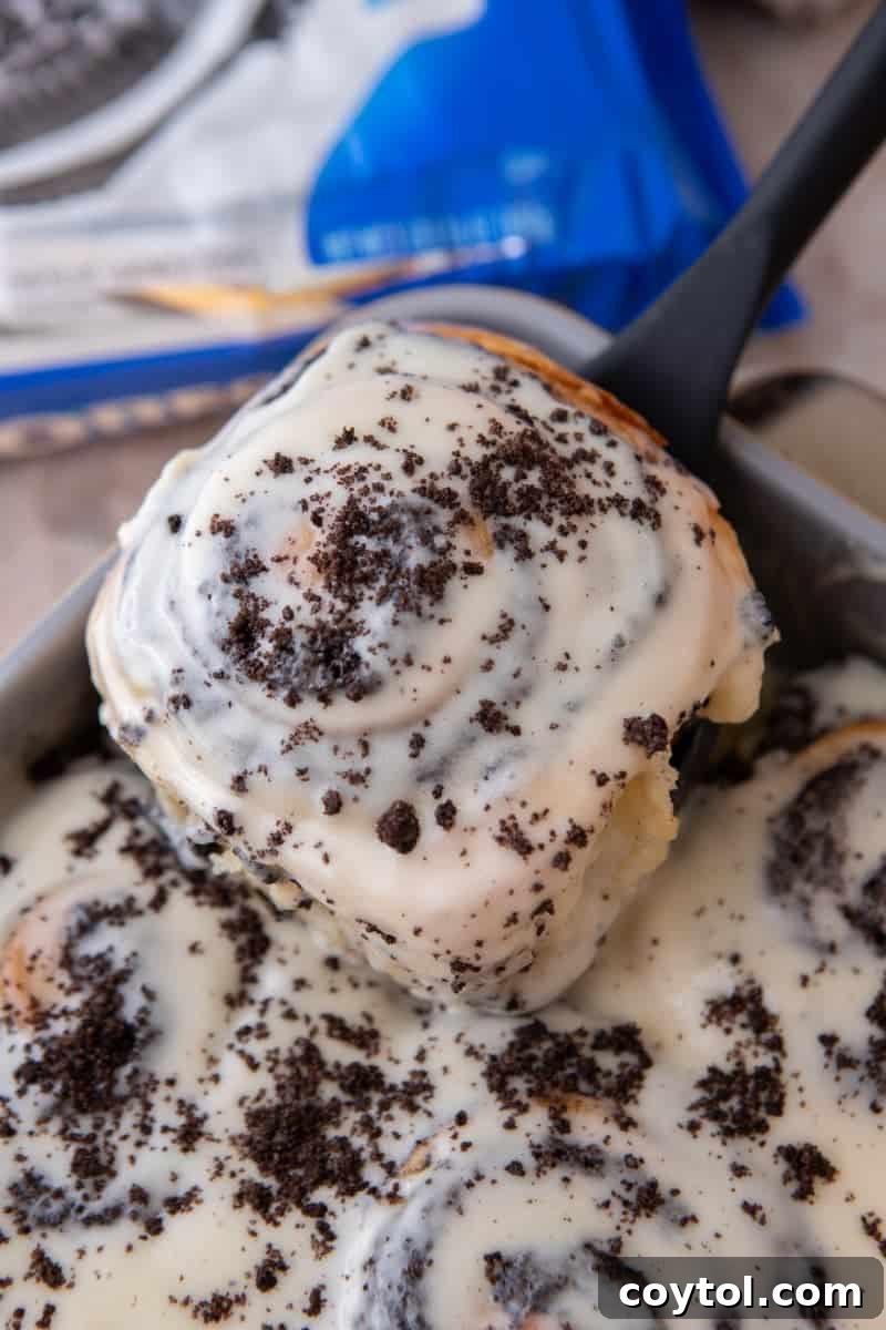 Glazed Oreo cinnamon roll topped with crushed Oreos being lifted from the pan