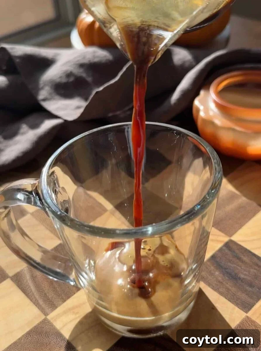 Hot espresso poured over two tablespoons of pumpkin spice sauce in a tall glass mug.